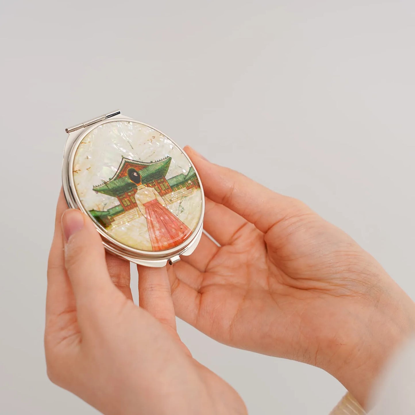 A compact mirror featuring a shimmering design of a person in a hanbok before a traditional Korean building