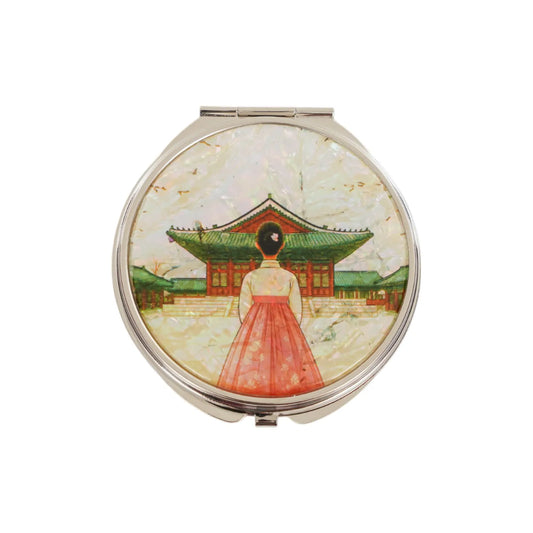 A compact mirror with an iridescent design of a hanbok-clad figure before a traditional Korean building