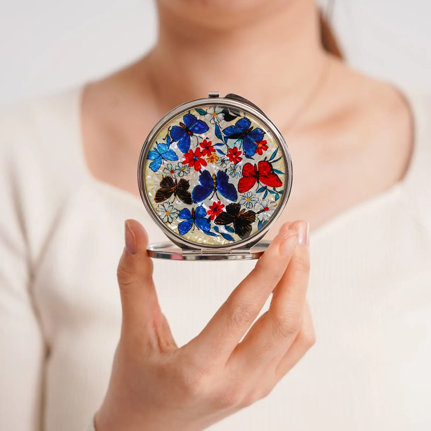 A compact mirror with a pearlescent background, decorated with colorful butterflies and flowers