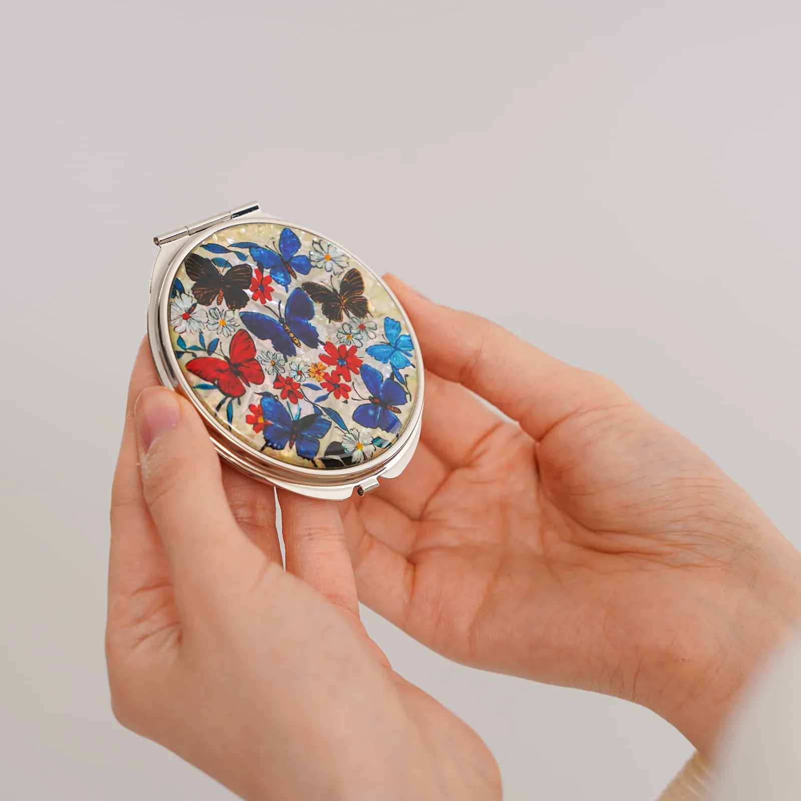 A compact mirror with a vibrant butterfly and floral design, featuring blue, red, and black butterflies