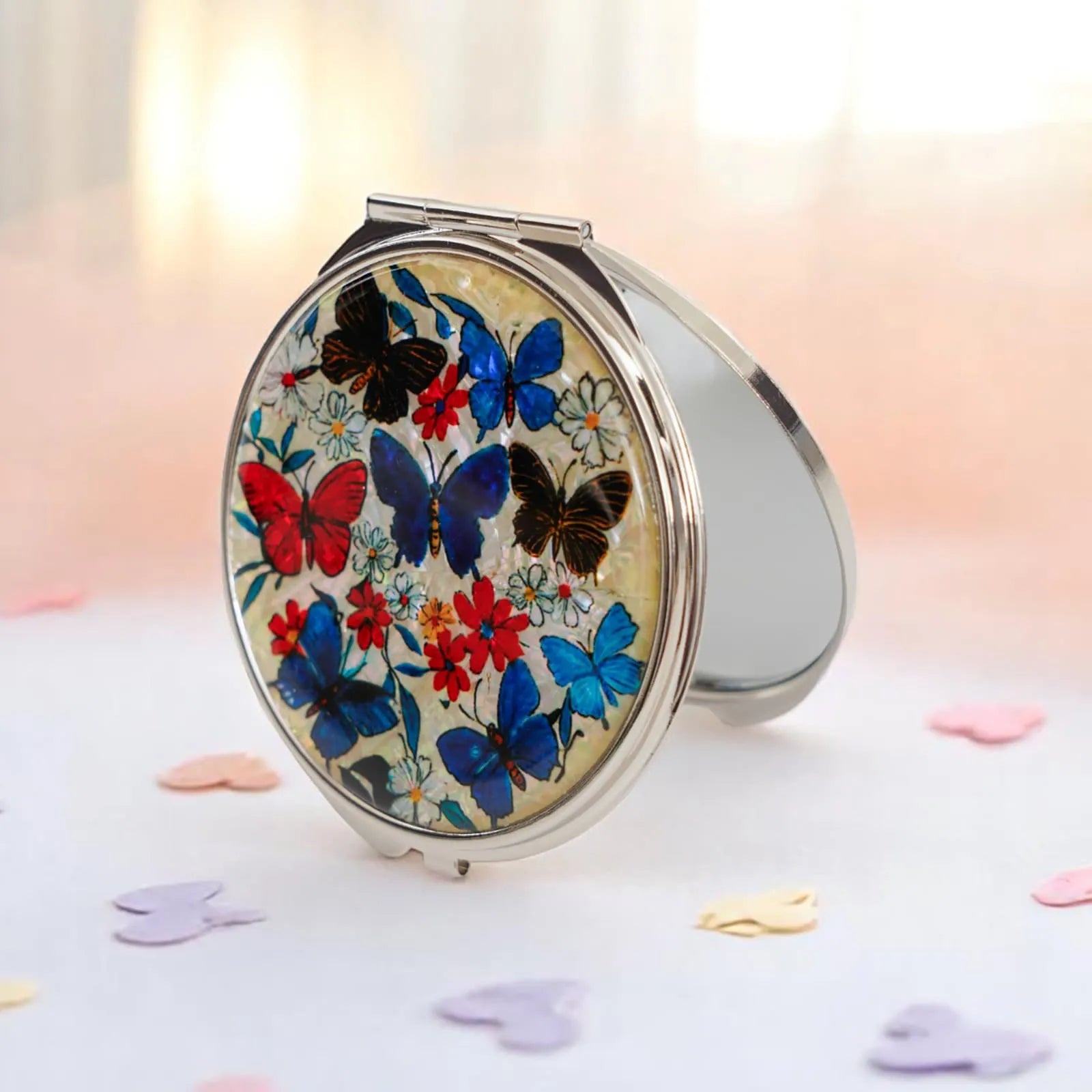 A compact mirror with a vibrant butterfly and floral design, surrounded by pastel heart-shaped confetti