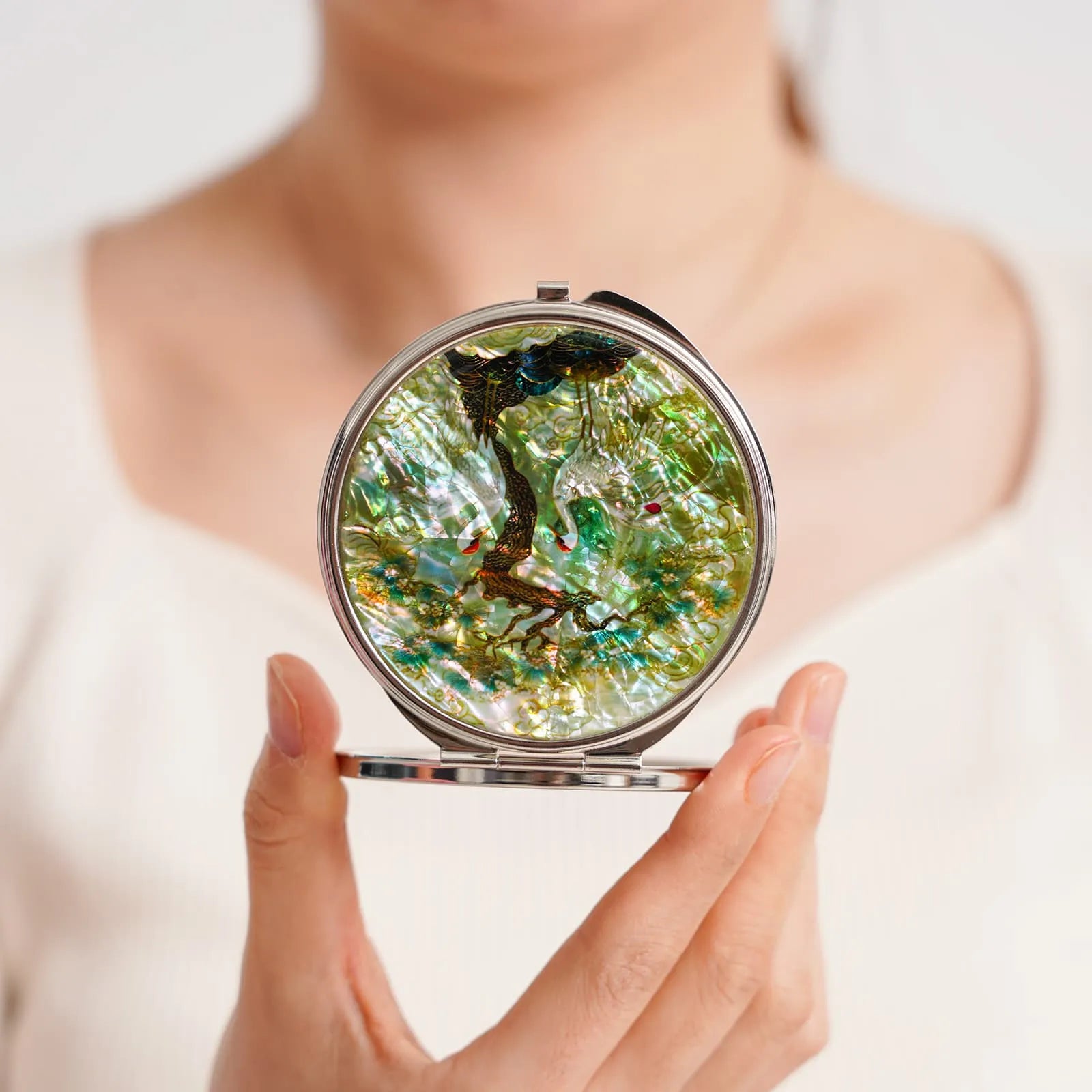A decorative compact mirror featuring pink and white lotus flowers with green leaves on a pearlescent surface