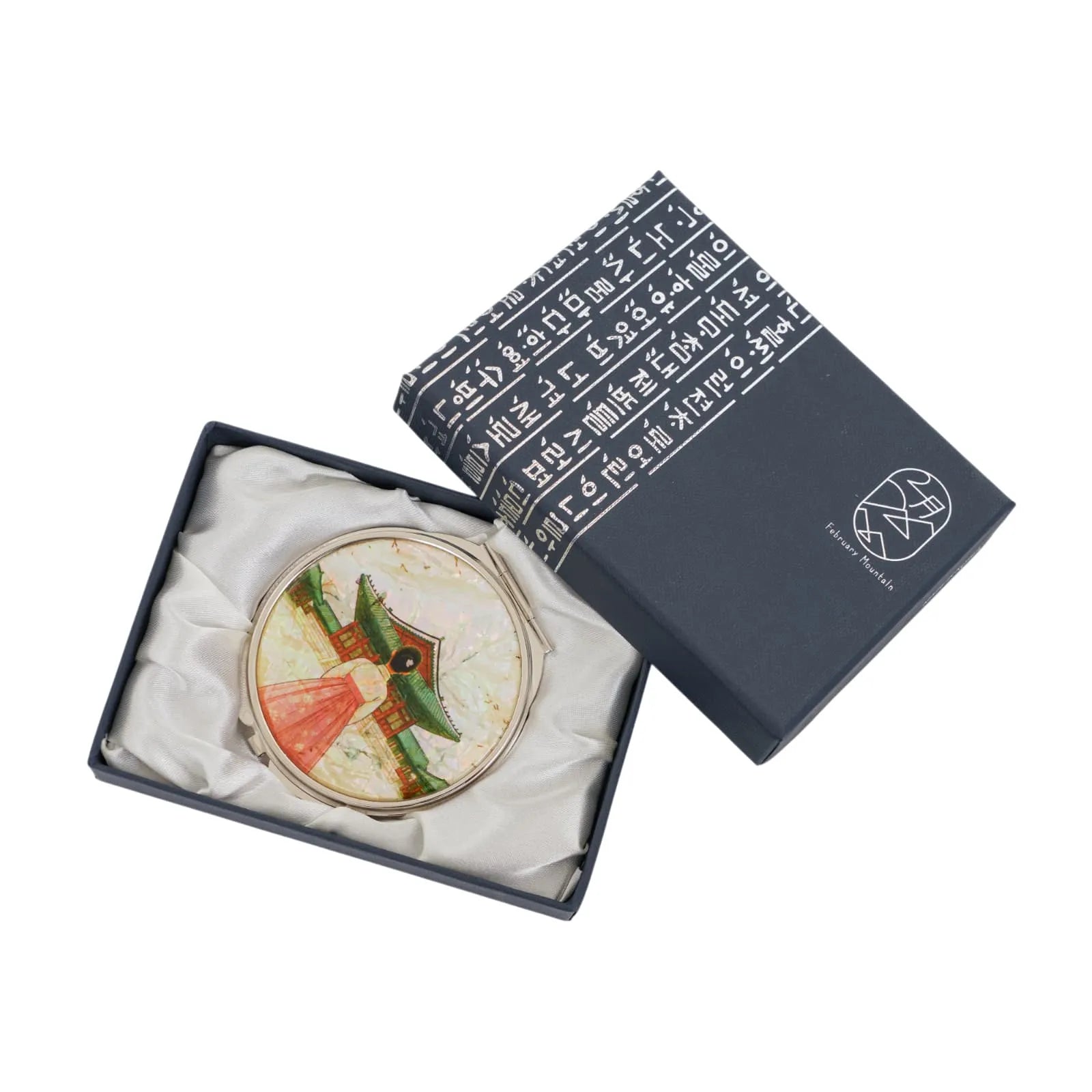 A decorative compact mirror with a traditional Korean design in a box with Korean script on the lid.