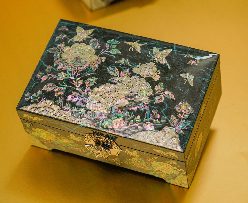 A decorative mother-of-pearl inlaid jewelry box with floral and butterfly motifs on a dark background, showcasing intricate craftsmanship and a metal clasp.