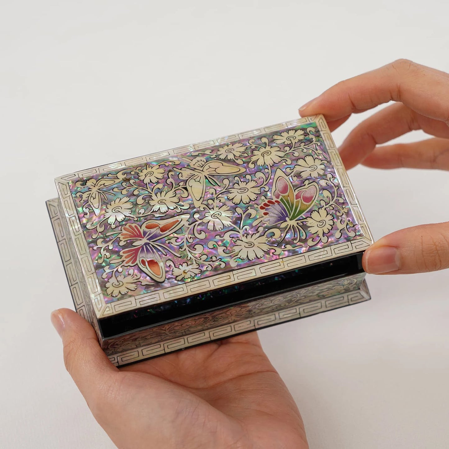 A hand holding an open Korean traditional Najeonchilgi jewelry box featuring intricate mother of pearl butterfly and floral inla