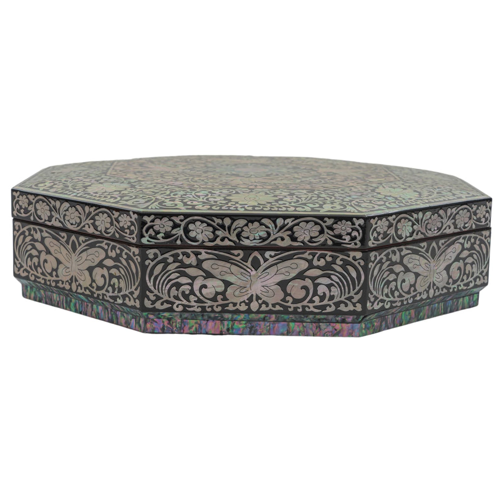 A low-profile octagonal black lacquer box with Mother of Pearl inlay showing detailed floral motifs, viewed from a side angle against a white backdrop.
