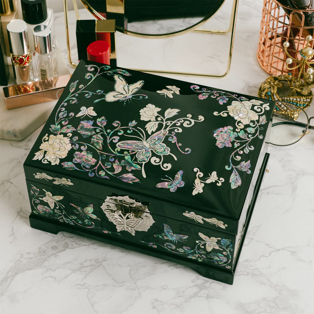 A mother-of-pearl box with floral and butterfly motifs on a marble countertop with cosmetics.