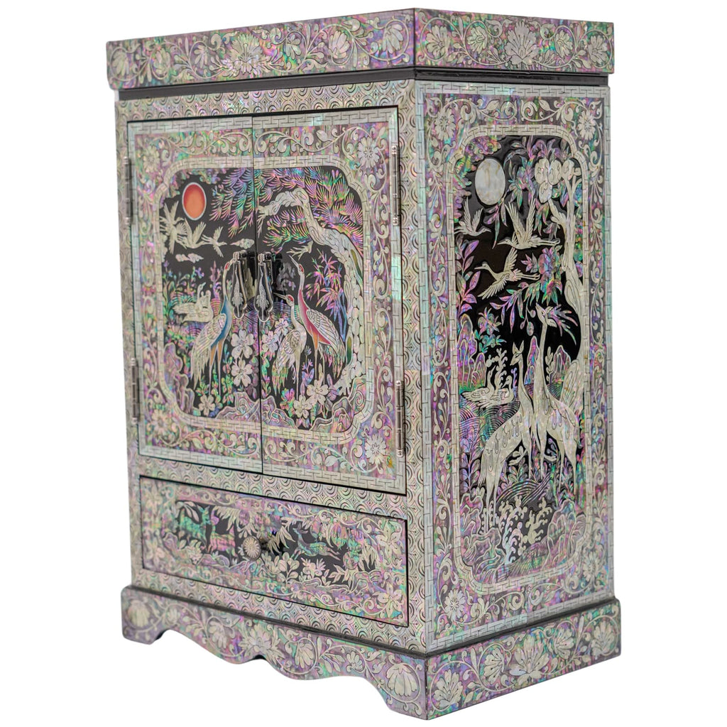 A mother-of-pearl inlaid cabinet showcasing a moon, cranes, and foliage against a dark background, with a scalloped base and ornate border.