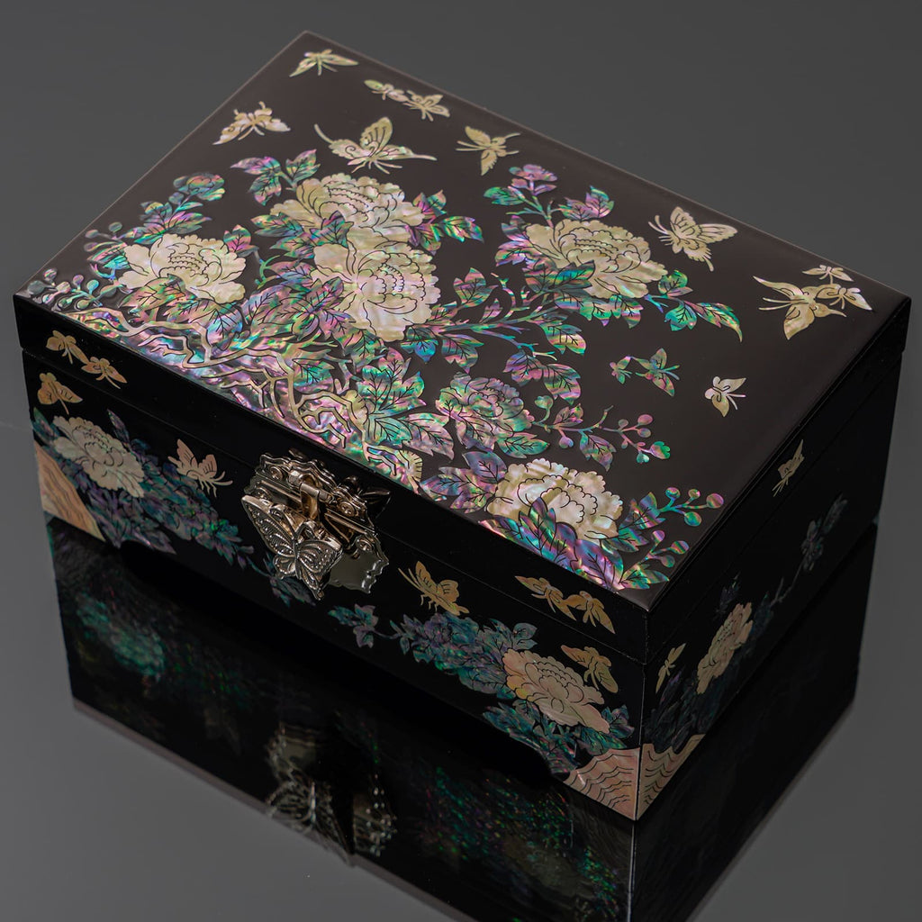 A mother-of-pearl jewelry box with a floral and butterfly design, reflecting on a dark surface.