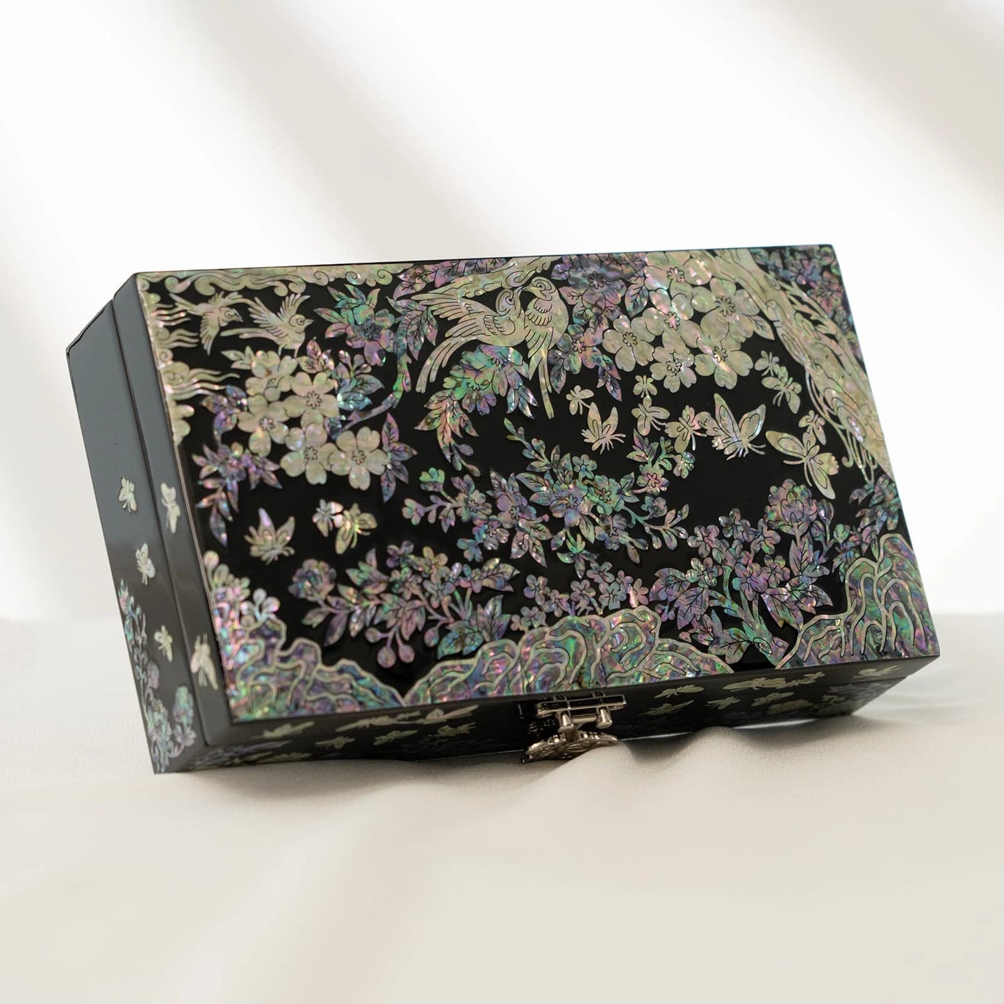 Angled shot of a premium black lacquer box adorned with vibrant mother-of-pearl birds, blossoms, and butterflies against a soft backdrop