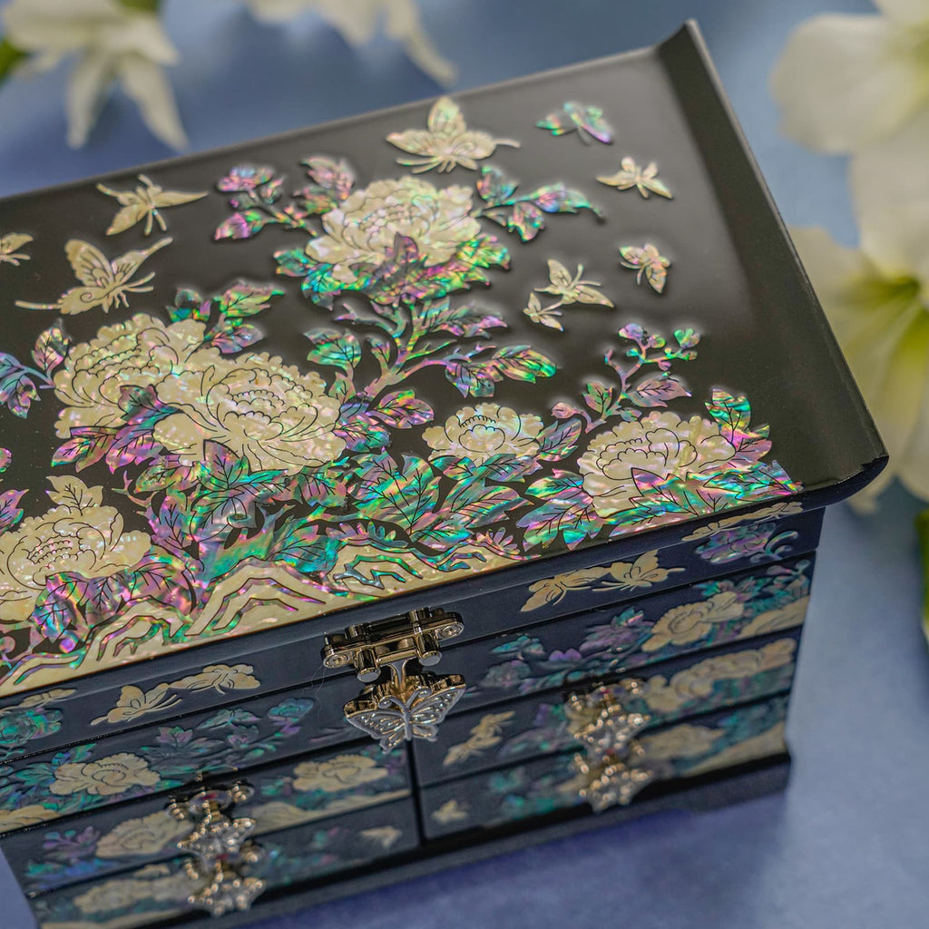 An intricately inlaid mother-of-pearl jewelry box with vibrant floral patterns on a dark background, positioned against a blue surface.