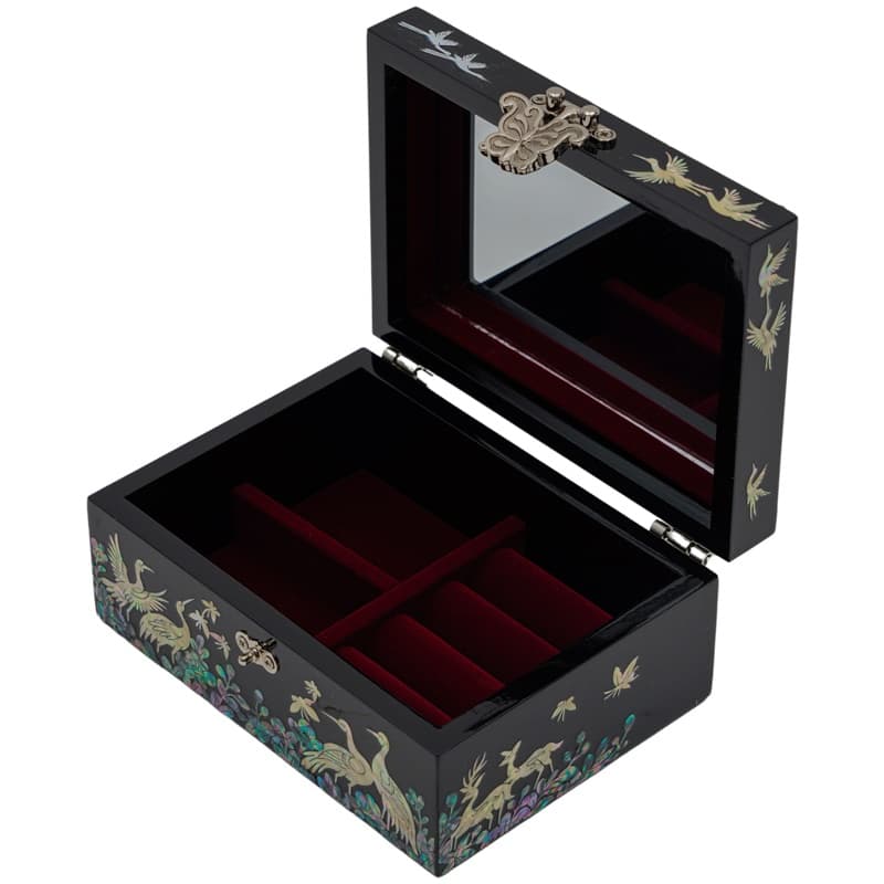 An open black lacquer box with mother-of-pearl crane inlays and a mirrored lid, featuring a red velvet interior with compartments, showcasing Asian artistry.