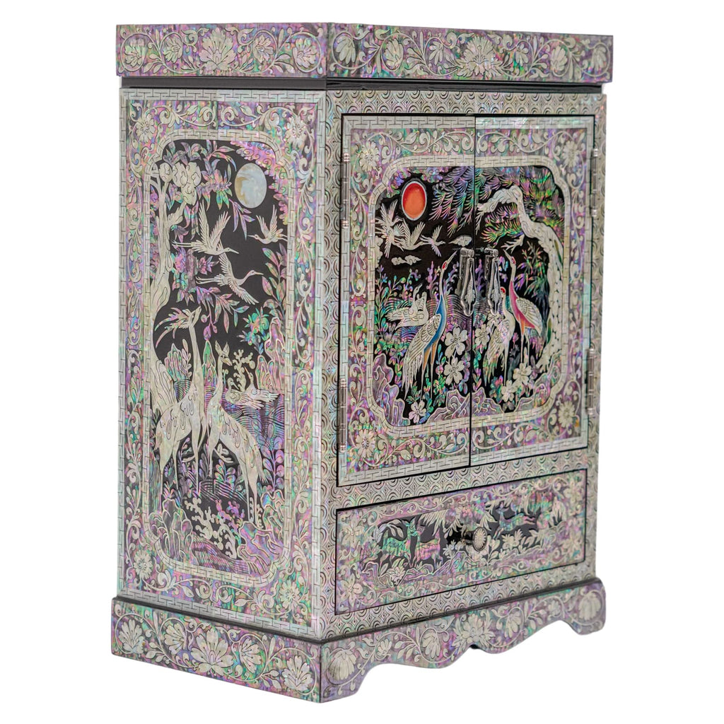 An ornate mother-of-pearl cabinet featuring a celestial theme with a sun and moon amidst cranes and lush foliage on a scalloped base.