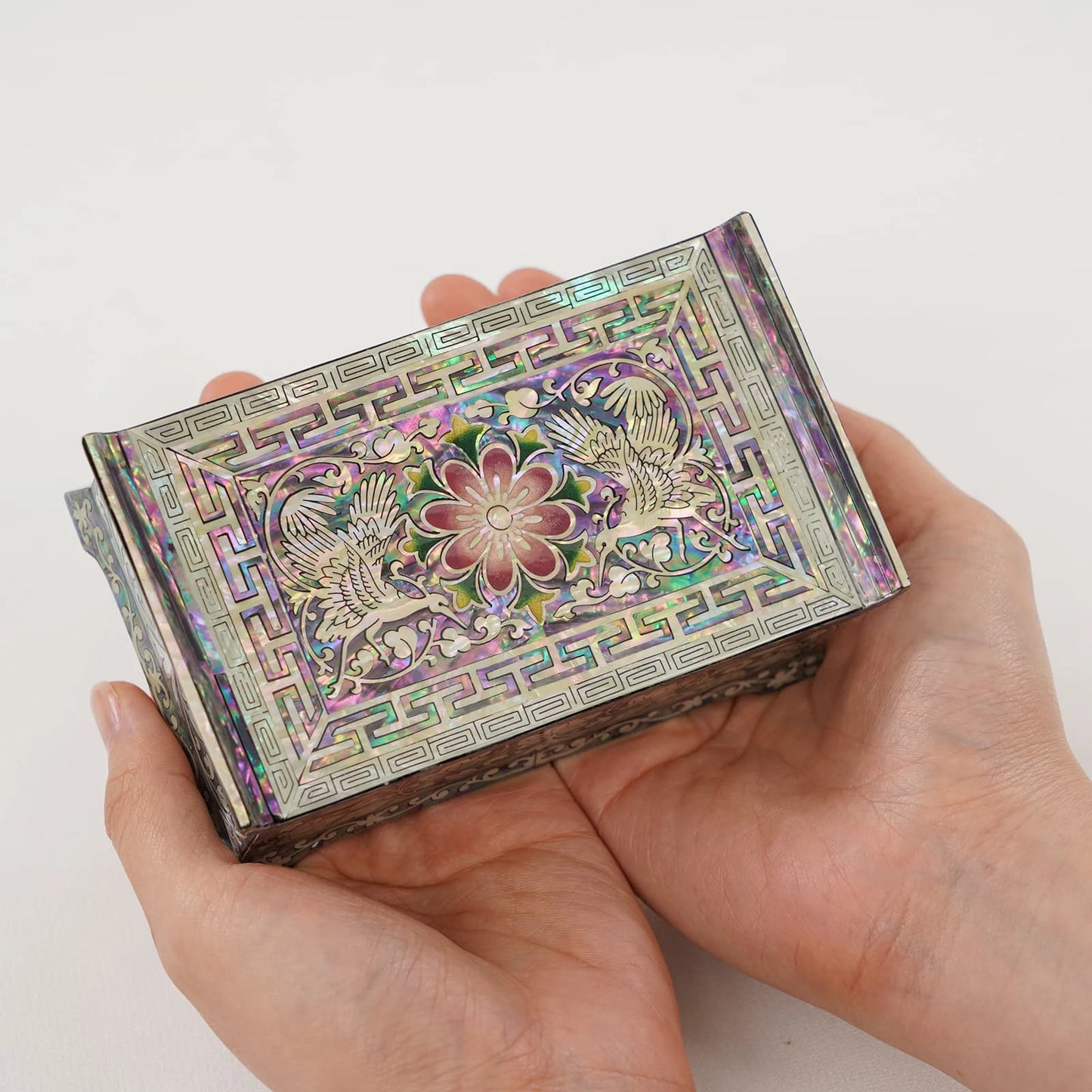 A pair of hands holding a small Korean Mother of Pearl box. Demonstrates the scale and intricate crane pattern of this traditional handmade gift