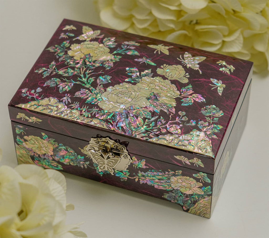 A purple mother-of-pearl inlaid jewelry box with floral designs and a metal clasp, displayed alongside white flowers.
