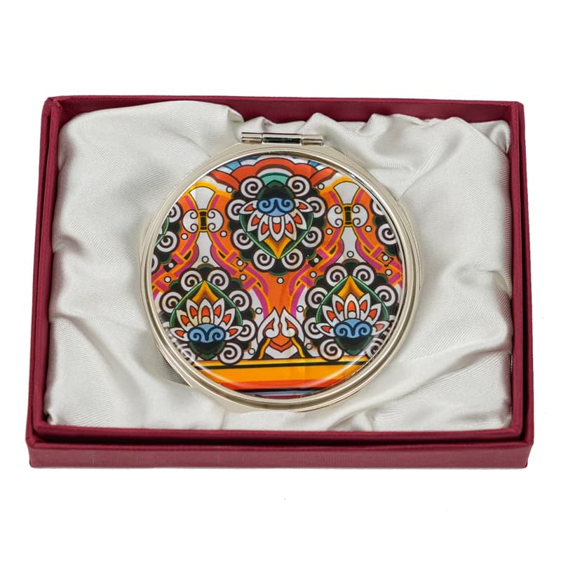 A round compact mirror featuring a vibrant, multicolored, paisley and floral pattern, presented in a burgundy box with a satin interior