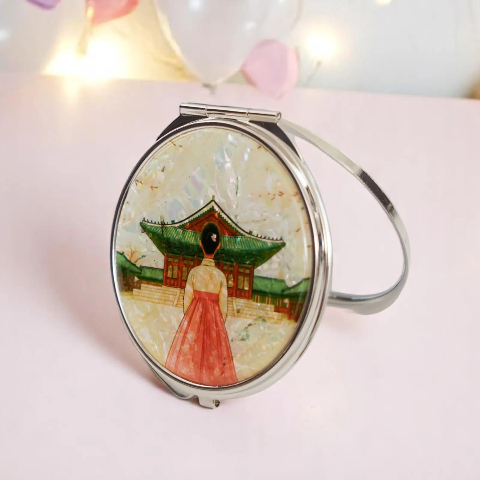 A round compact mirror featuring a woman in a hanbok, set against a traditional Korean palace backdrop