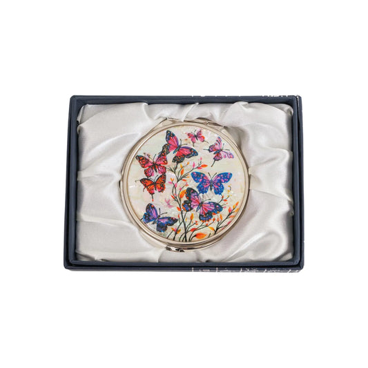 A round compact mirror with a vibrant design featuring colorful butterflies and delicate flowers, placed inside a white satin-lined box