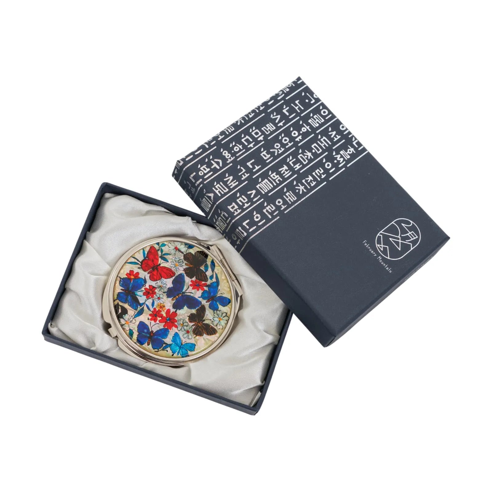 A round compact mirror with colorful butterfly and flower designs, placed inside a satin-lined gift box.