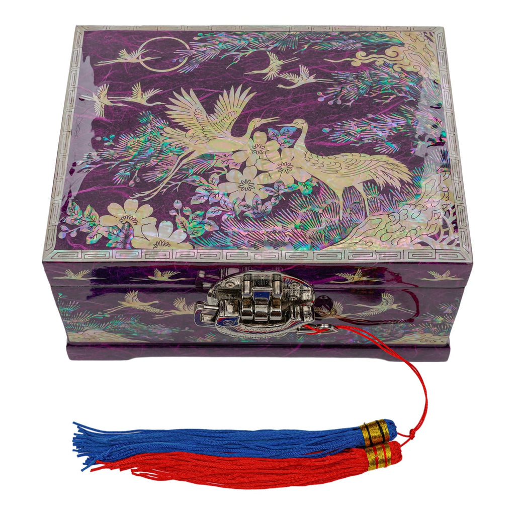 A square mother-of-pearl inlaid box with a detailed design of cranes and flowers on a purple background, featuring a metallic latch and a red string with a blue and red tassel attached.