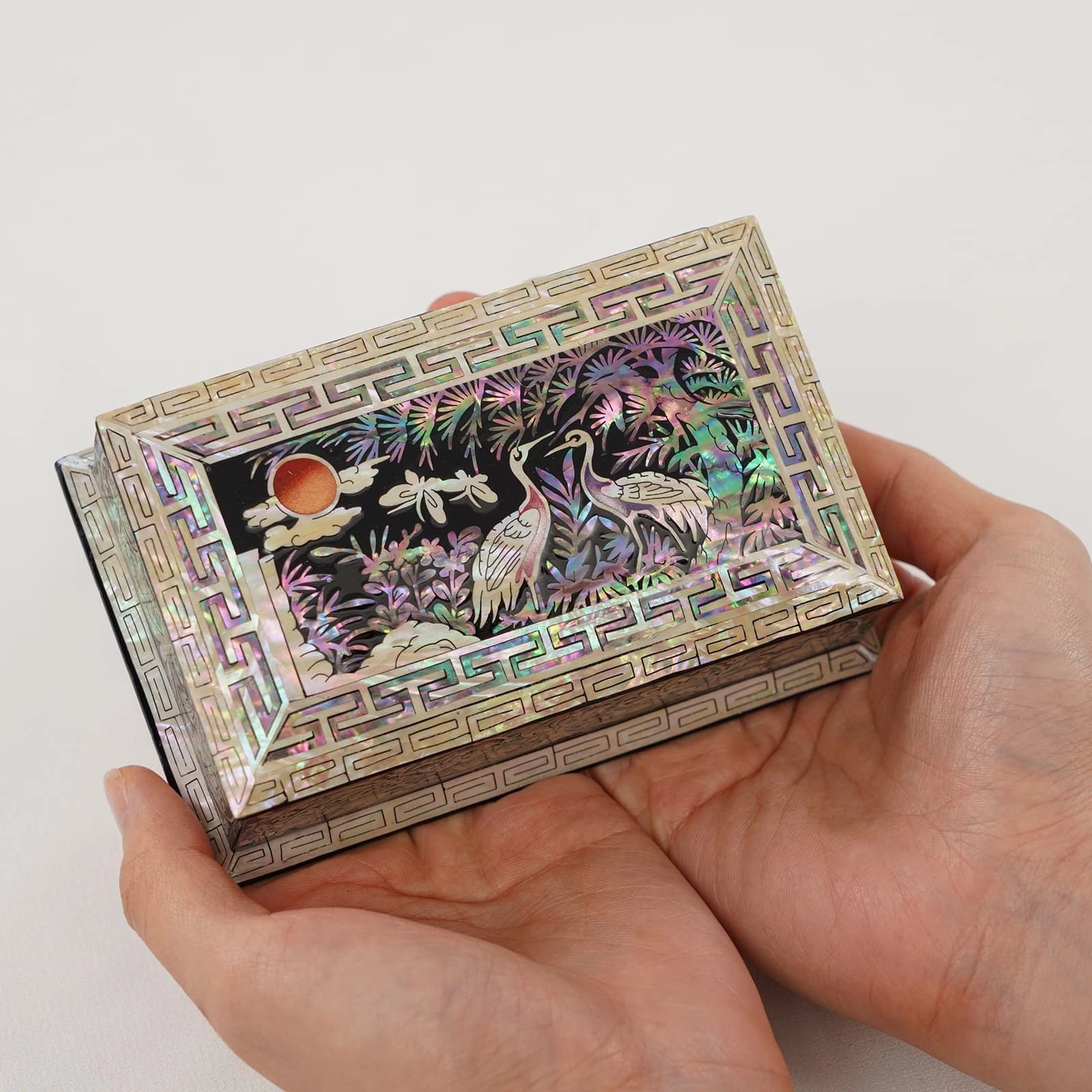A top-down view of a rectangular Najeonchilgi keepsake box held in two hands, showcasing a stunning mother of pearl inlay of cra