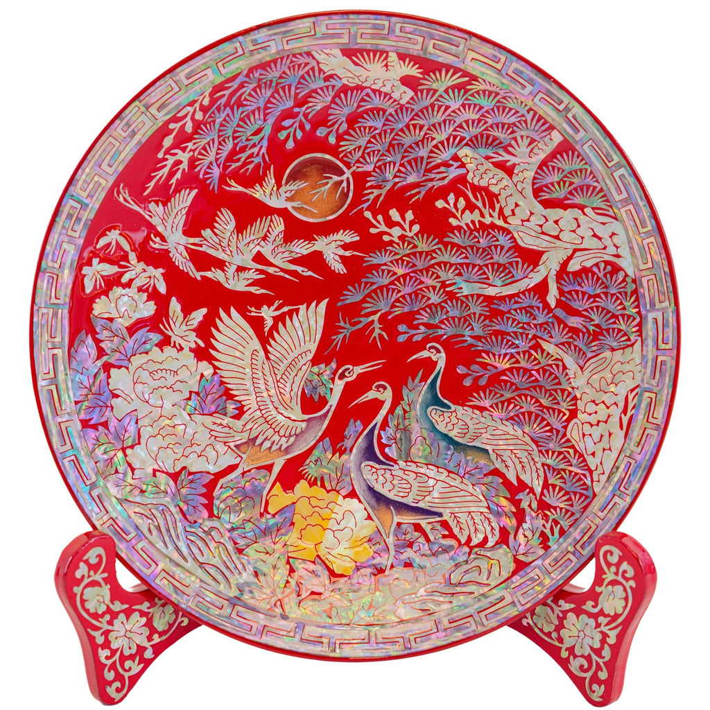 A vibrant red decorative plate with white cranes and multicolored floral patterns, complemented by a red stand with intricate designs