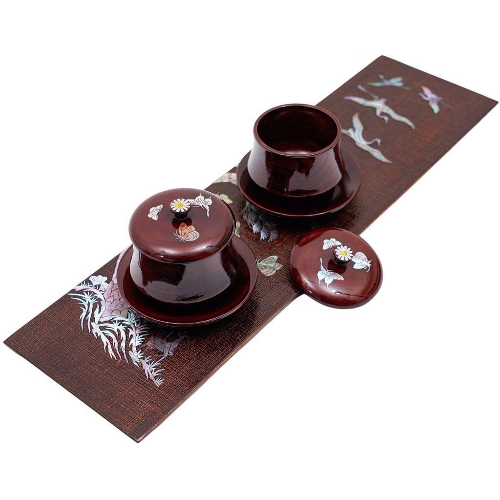 A wooden board with mother-of-pearl inlay displaying birds and flowers, with traditional Korean bowls.