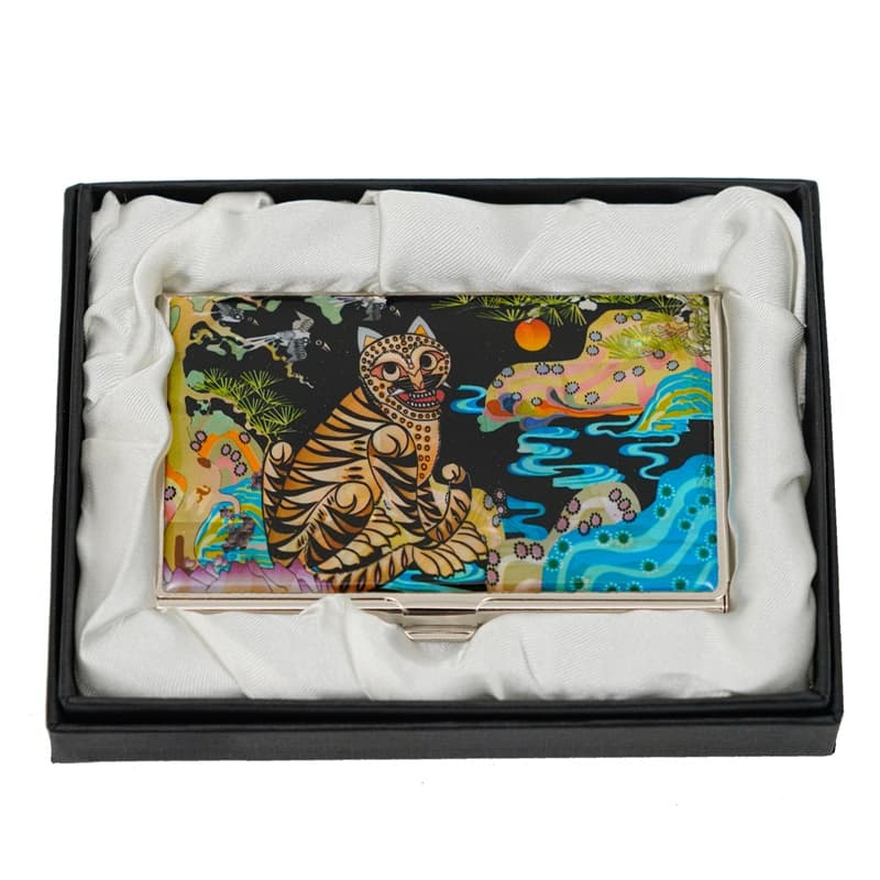 A business card case with a colorful tiger and whimsical scenery on its cover, in a black box with a white lining, designed for aesthetic appeal and functionality.