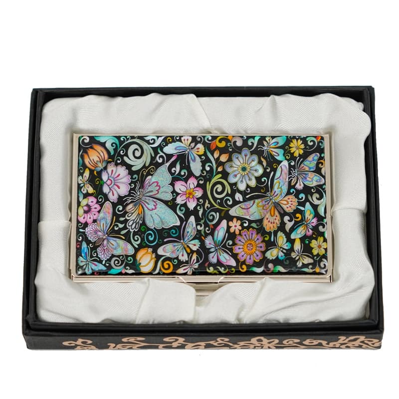 A business card holder features a black background with colorful butterflies and floral patterns, encased in a black gift box with white satin interior.