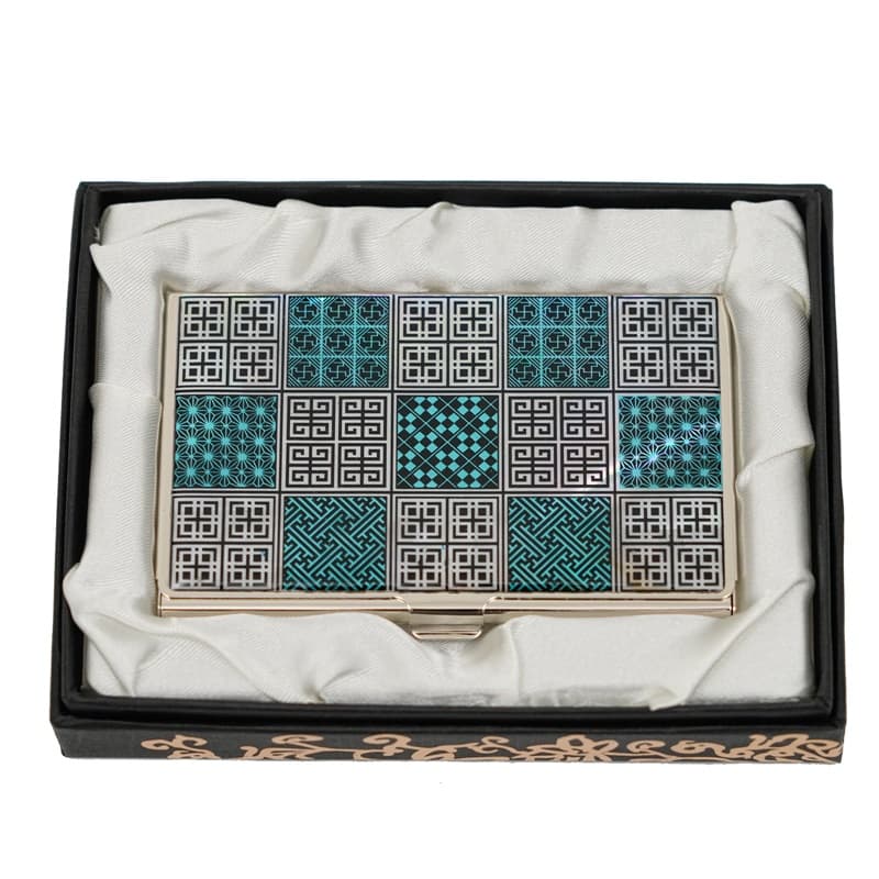 A business card case featuring a pattern of black and turquoise geometric designs, displayed within a black presentation box with a white satin lining.