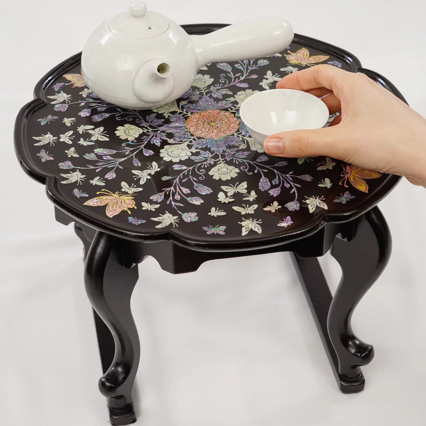 Black lacquer mother of pearl tray table with white ceramic teapot and teacup, decorative floral inlay and curved wooden legs