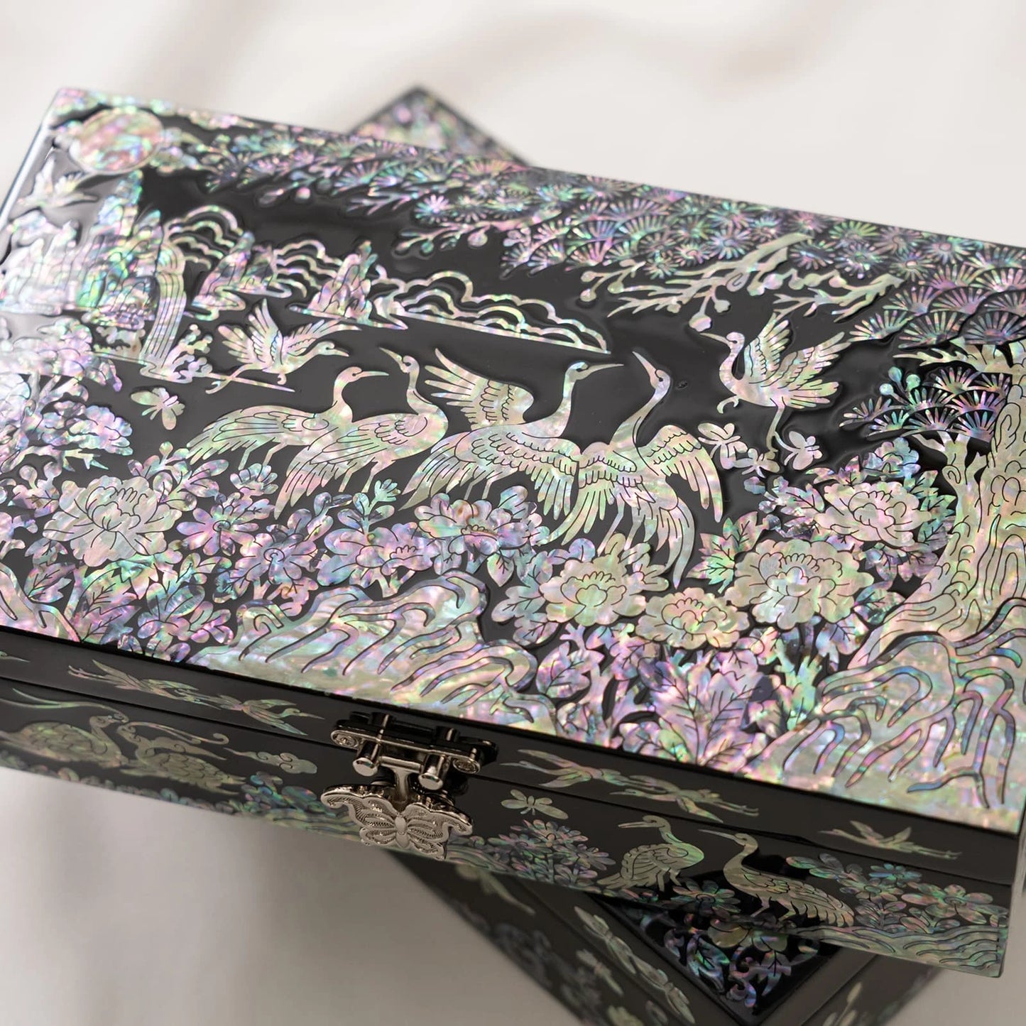 Close-up of a black lacquer box featuring detailed, shimmering mother-of-pearl inlays of cranes, pine trees, and a butterfly metal clasp