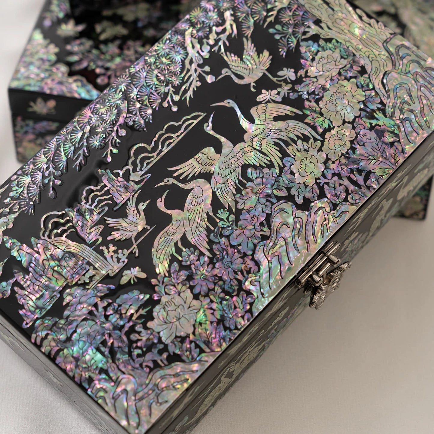 Close-up of a black lacquer box focusing on highly detailed iridescent crane and pine tree motifs with a butterfly metal clasp
