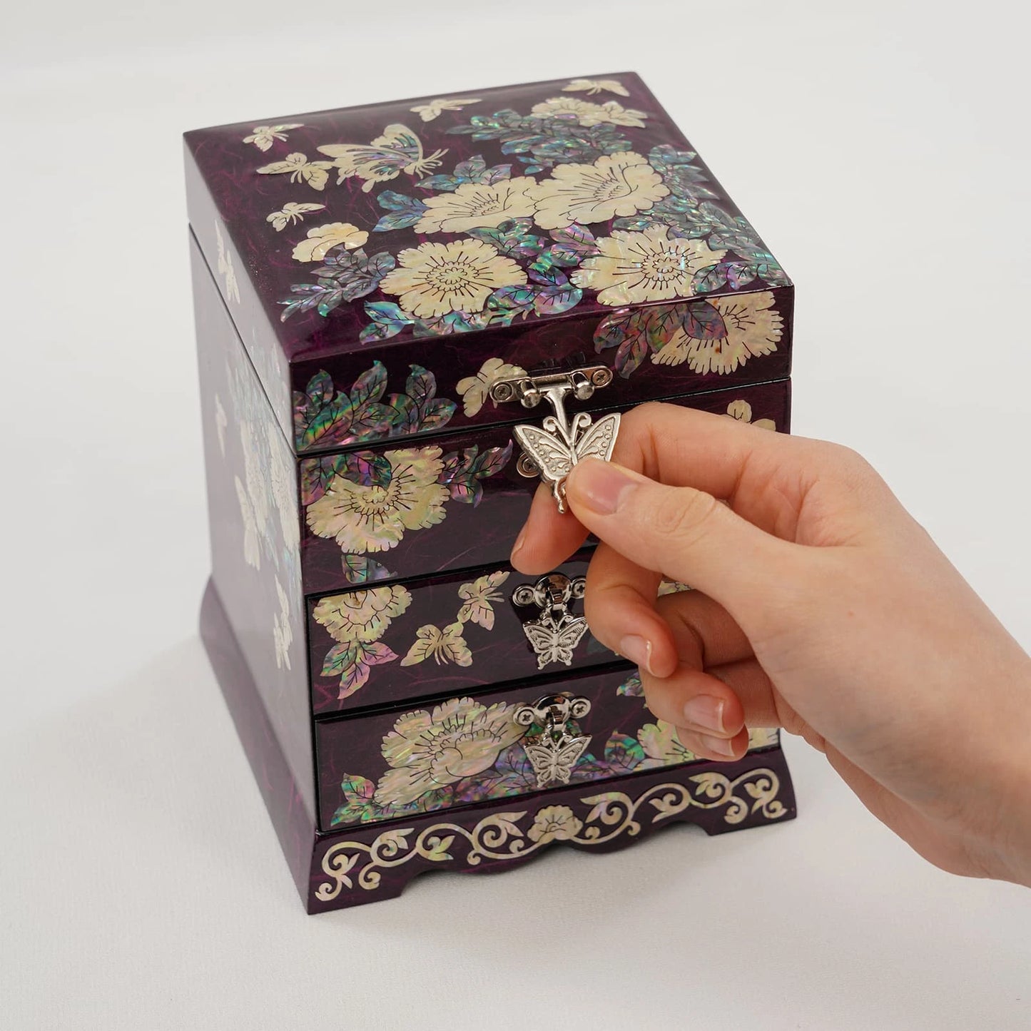 Close-up of hands lifting the lid of a decorative purple jewelry box. Showcasing iridescent shell work and an intricate butterfly clasp.
