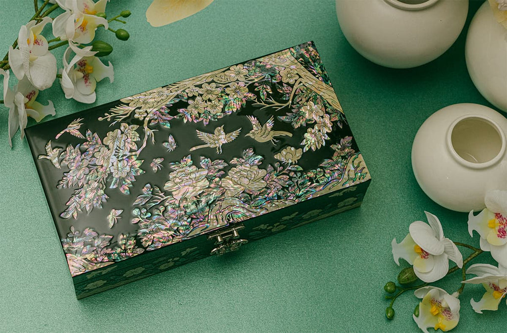 Elegant mother-of-pearl jewelry box on a green surface, accompanied by white orchids and ceramic vases.