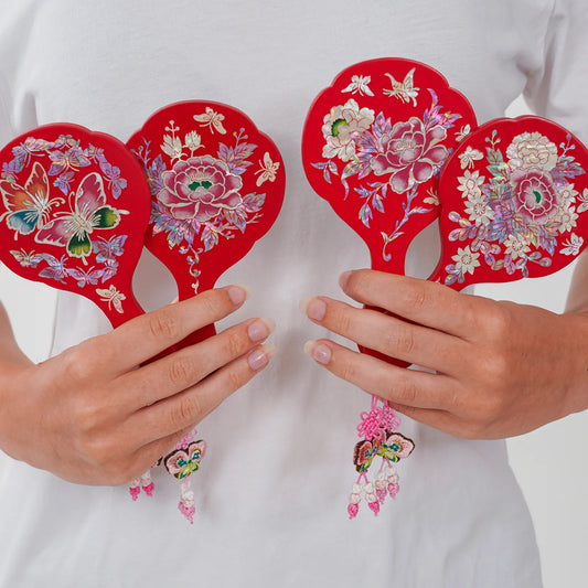 Four red floral and butterfly hand mirrors with tassels held in hands