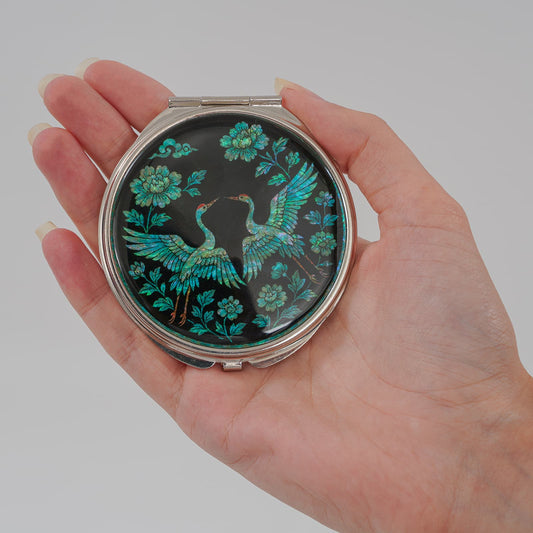 Hand holding compact mirror with cranes and peony floral design on black mother-of-pearl finish