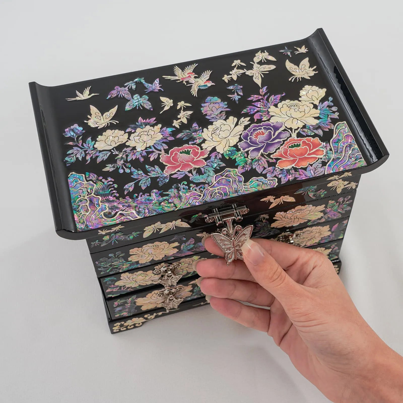 Hand opening butterfly clasp on mother-of-pearl floral jewelry box