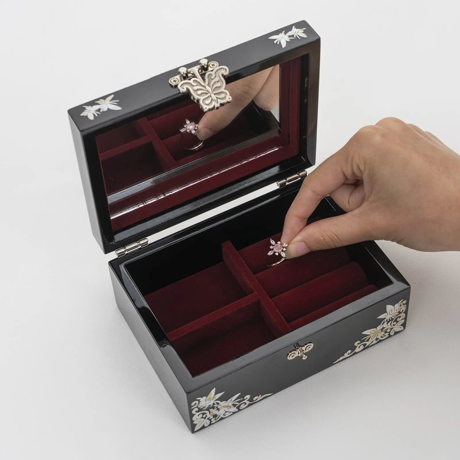 Hand placing ring inside a velvet-lined jewelry box with interior mirror and divider