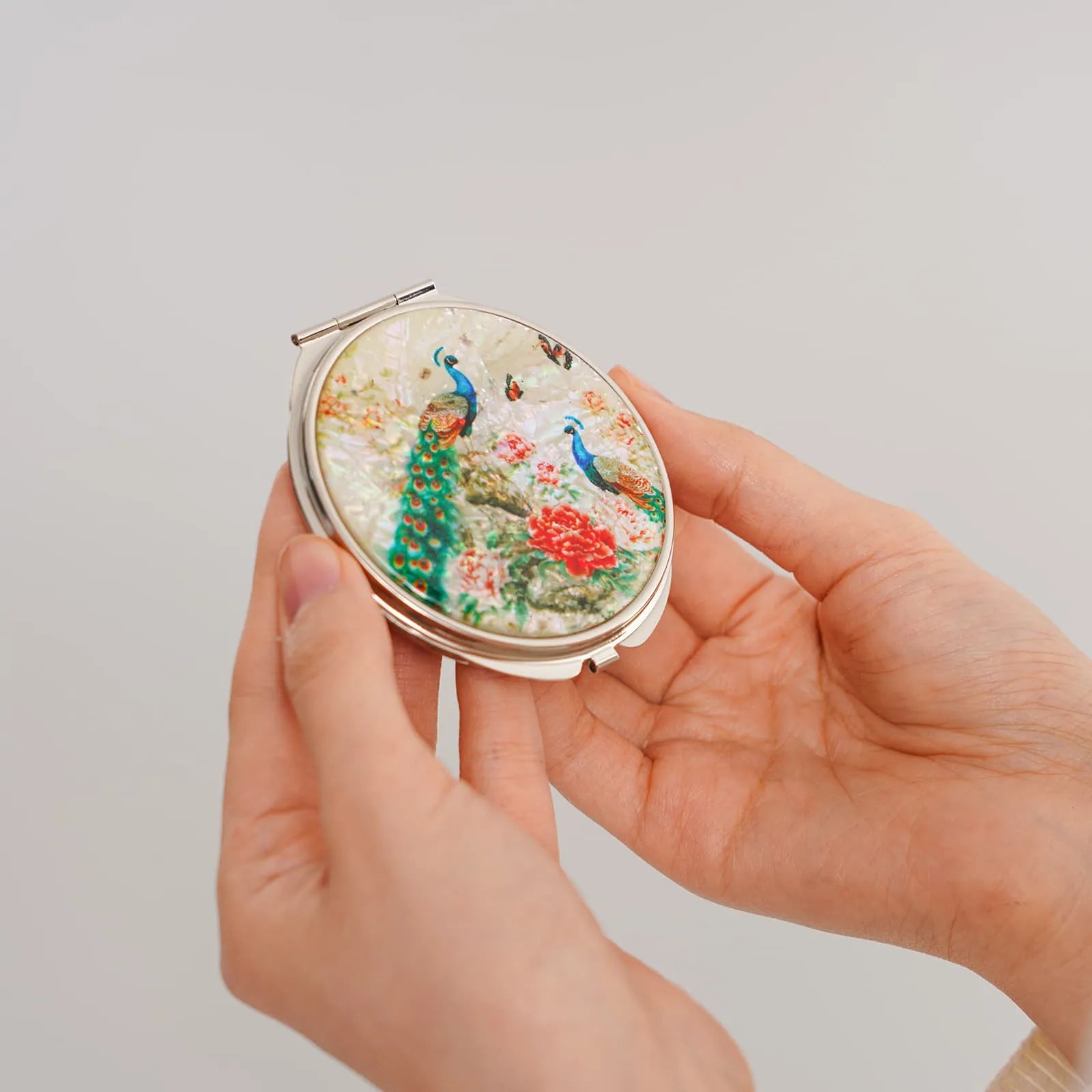 Hands holding a round compact mirror with peacocks and floral mother-of-pearl inlay