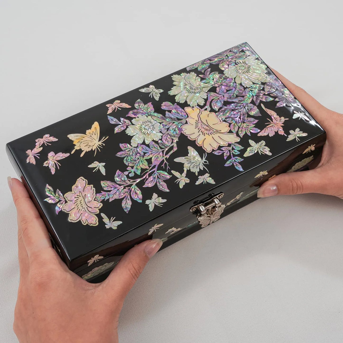 Hands holding black lacquer jewelry box with floral and butterfly inlay