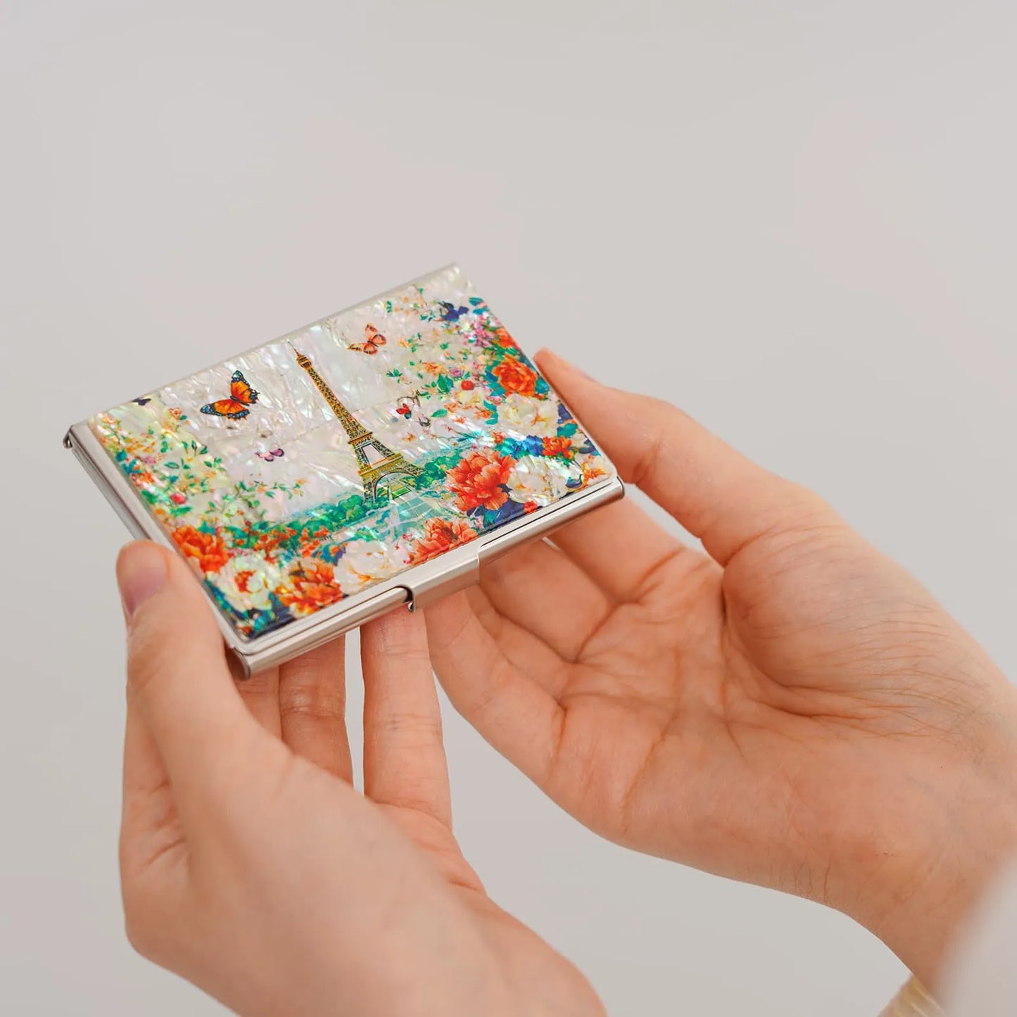 Hands holding floral Eiffel Tower card case against a plain background