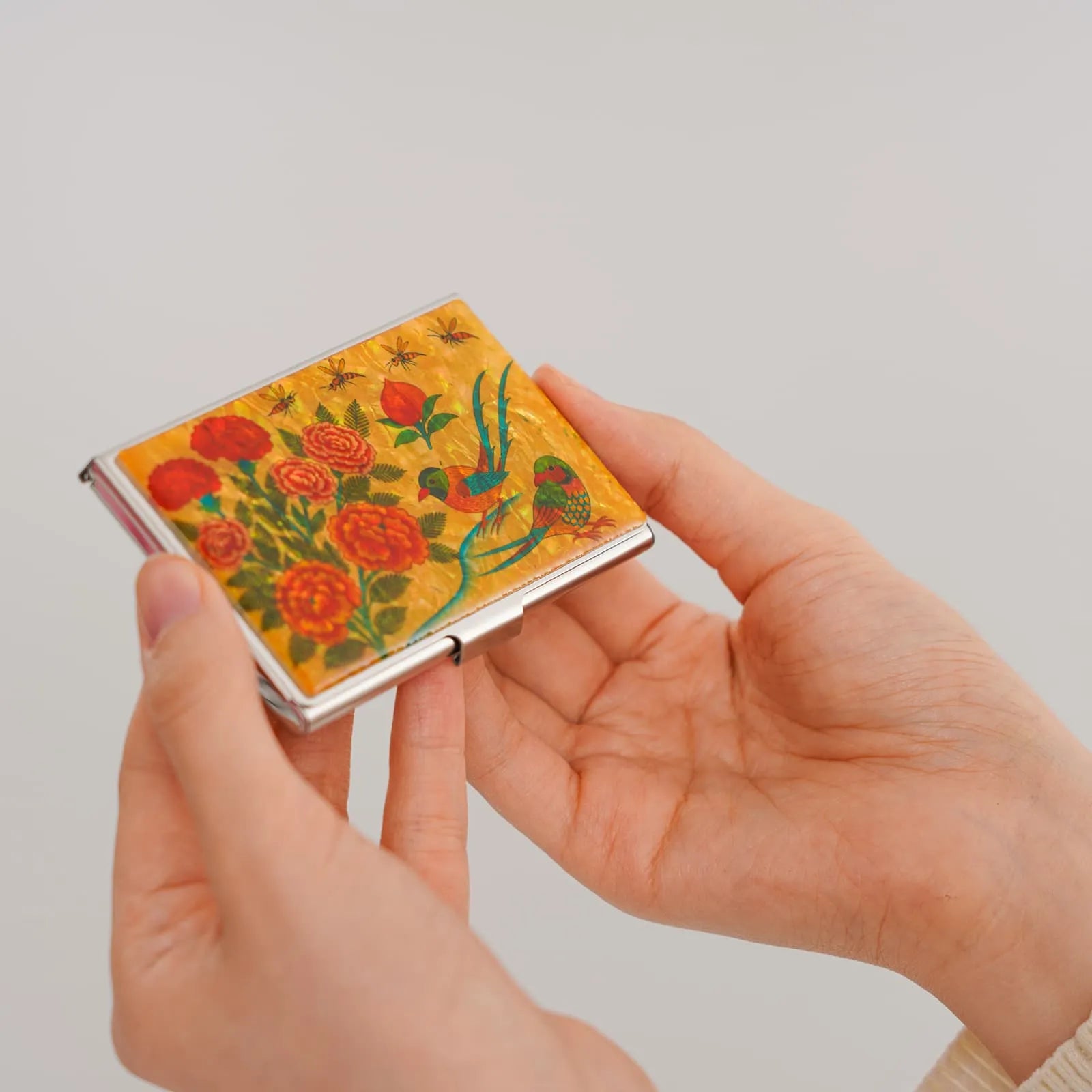 Hands holding golden card case with red flowers, birds, and mother-of-pearl shine