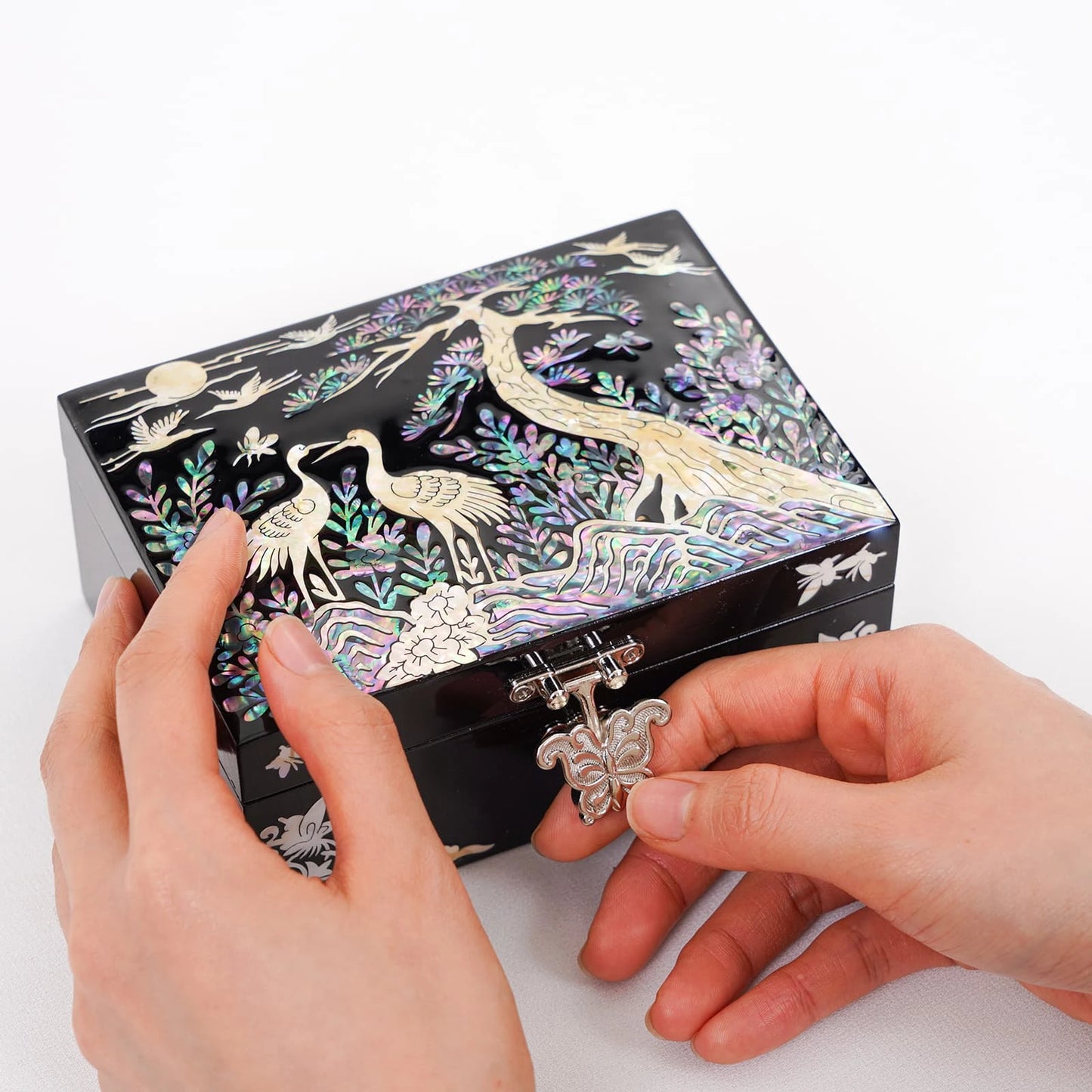 Hands opening black lacquer mother of pearl vanity jewelry box with crane design, secure metal latch and handcrafted Korean craftsmanship