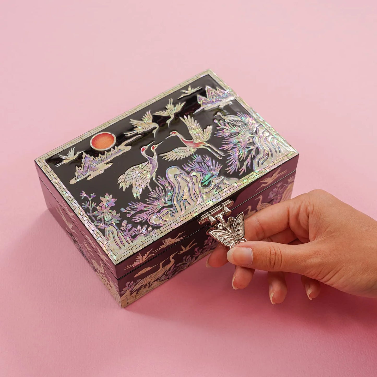 Hand turning butterfly clasp on crane mother-of-pearl box with sunset motif