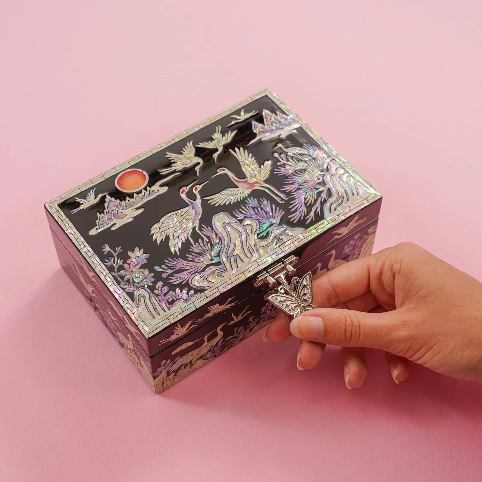 Hand turning butterfly clasp on crane mother-of-pearl box with sunset motif