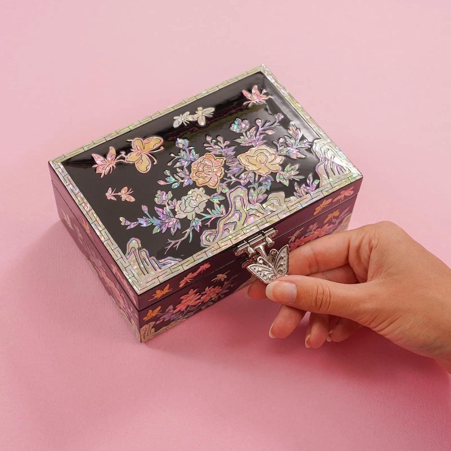Hand unlocking floral mother-of-pearl box with butterfly clasp on pink background