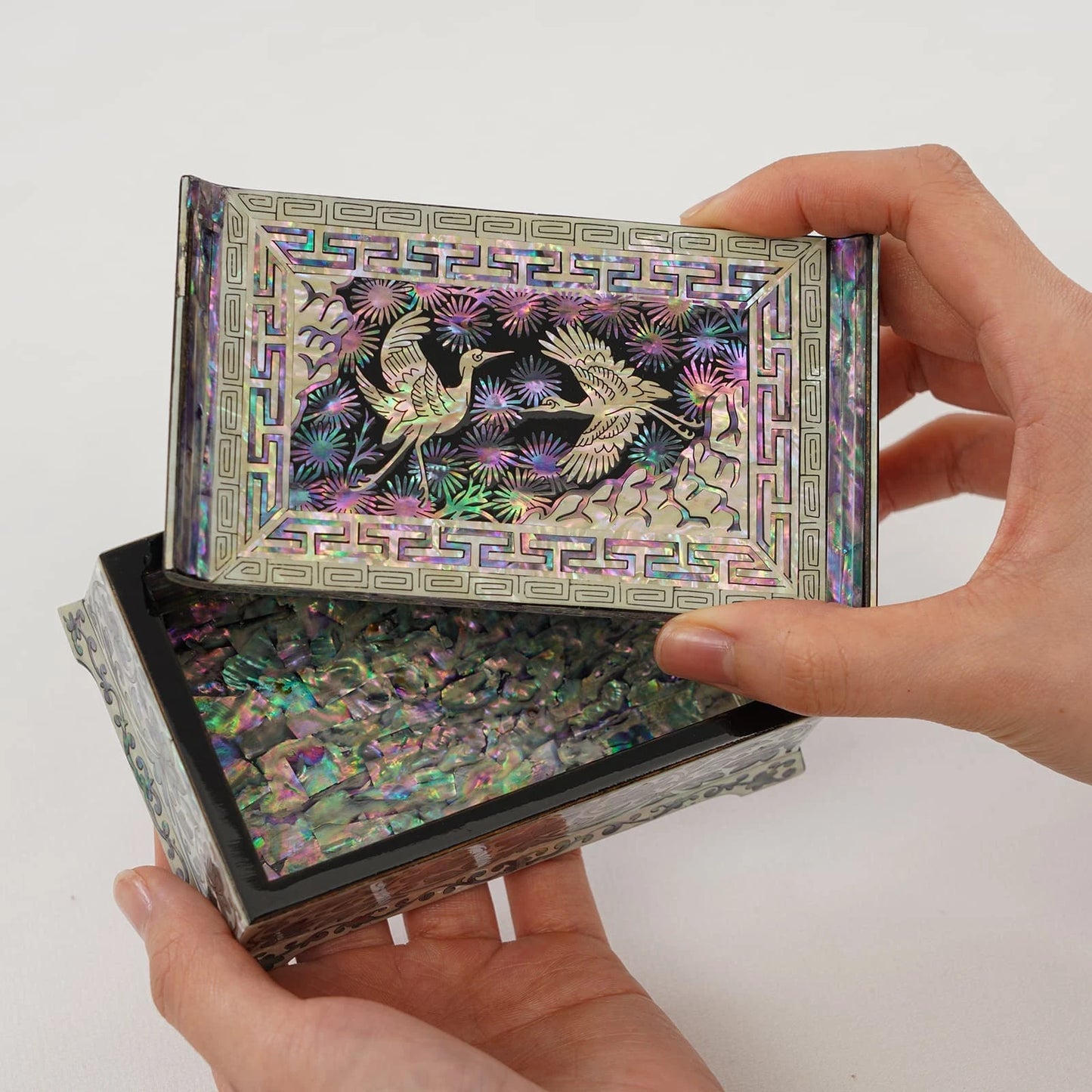 High-angle view of a luxury lacquer jewelry box showcasing the shimmering floral and crane artwork on the top and side panels