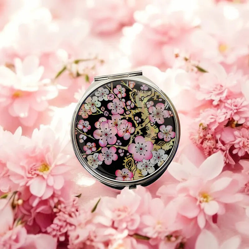 Mother-of-pearl compact mirror featuring a plum blossom design on a black background, surrounded by pink flowers