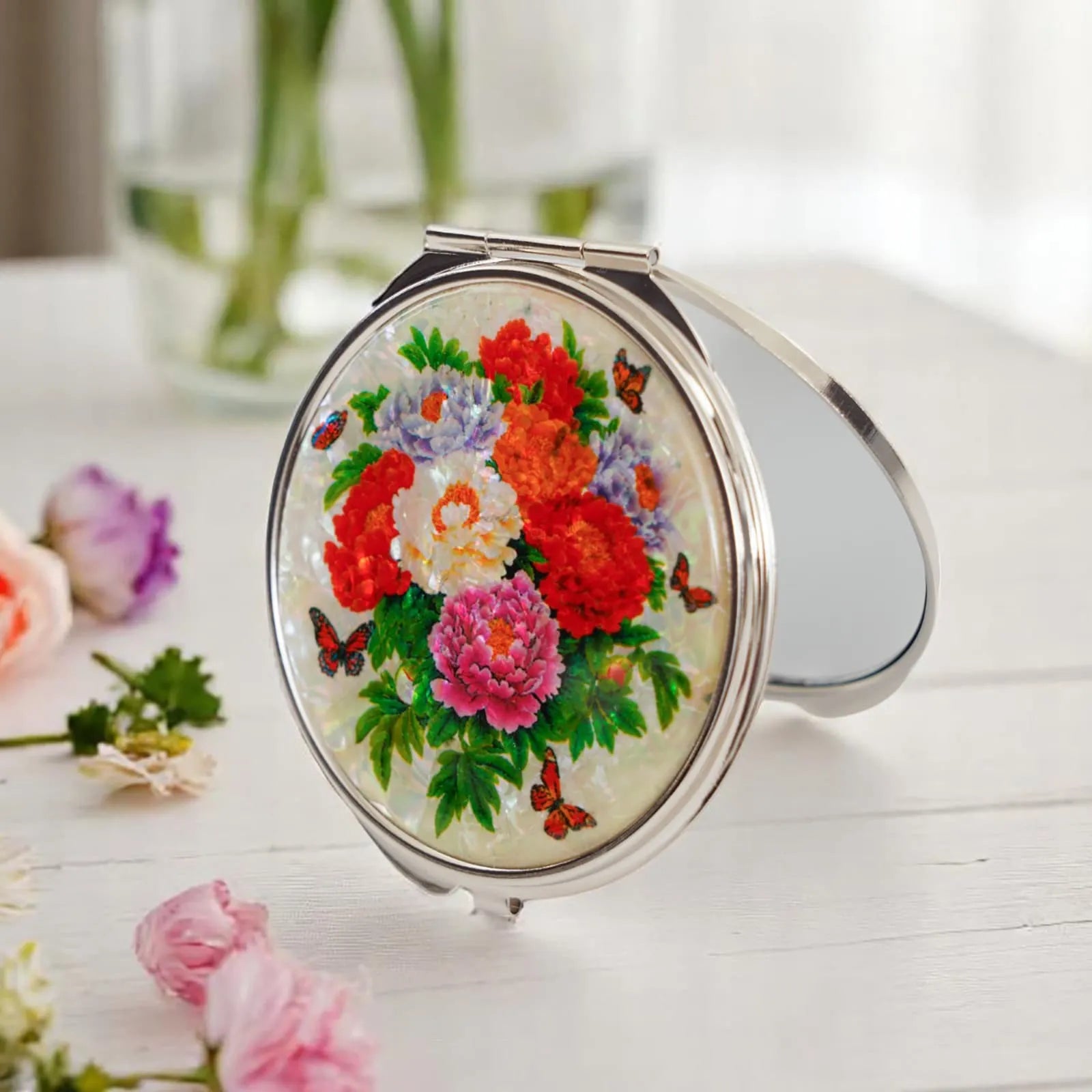 Mother-of-pearl compact mirror with vivid peony design on a festive table